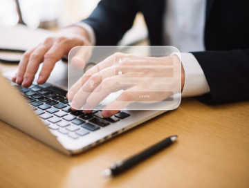 A person in business attire types on a laptop keyboard, with a transparent digital login interface overlayed on the image. A pen rests on the desk.