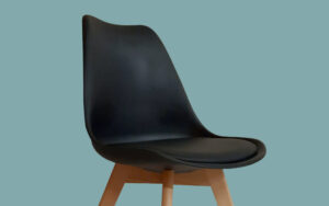 A modern black plastic chair with a curved seat and wooden legs, set against a plain light blue background.